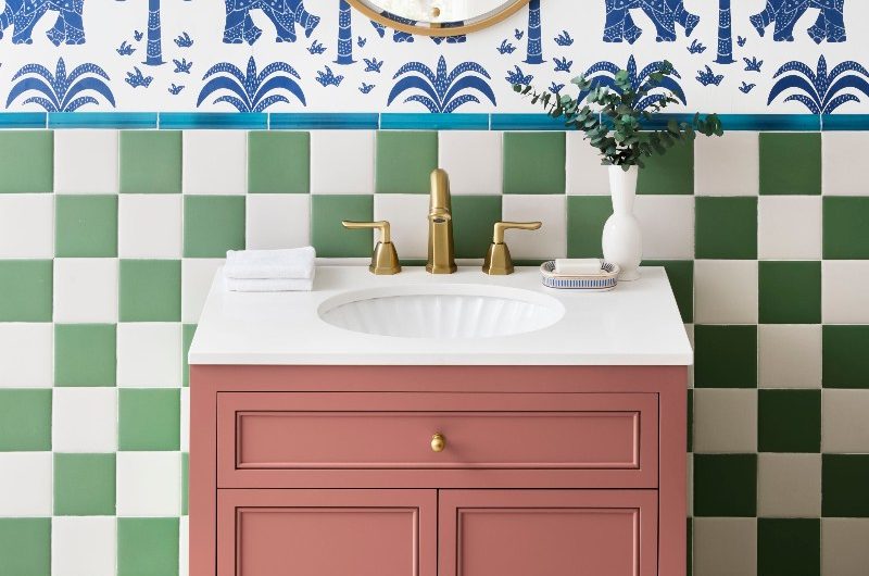 Colourful scheme with checkerboard tiles, patterned wallpaper, a dark pink vanity with an inset basin, and gold fittings.