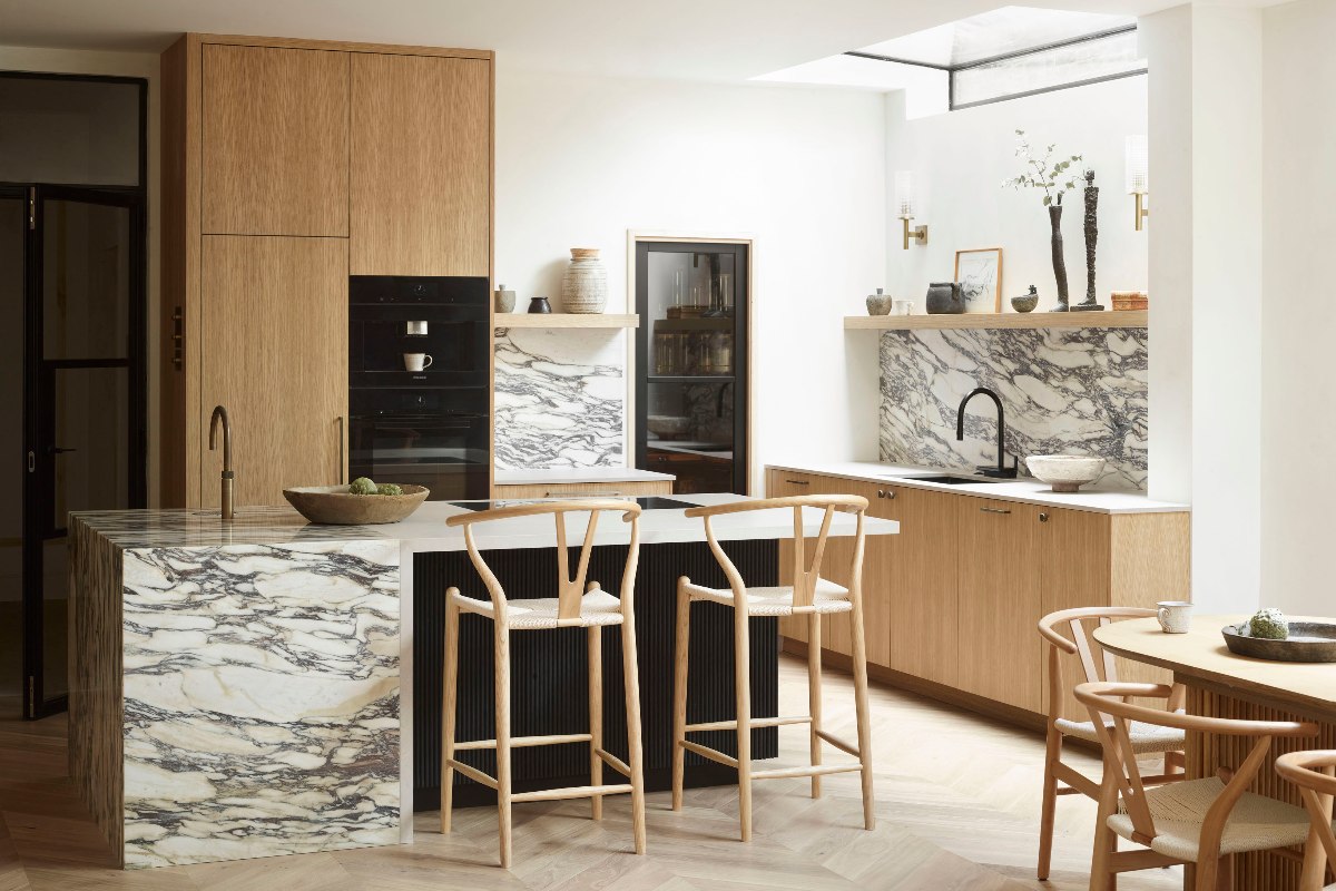 An L-shaped layout with wood cabinetry, marble surfaces, black finishes and an adjacent pantry.