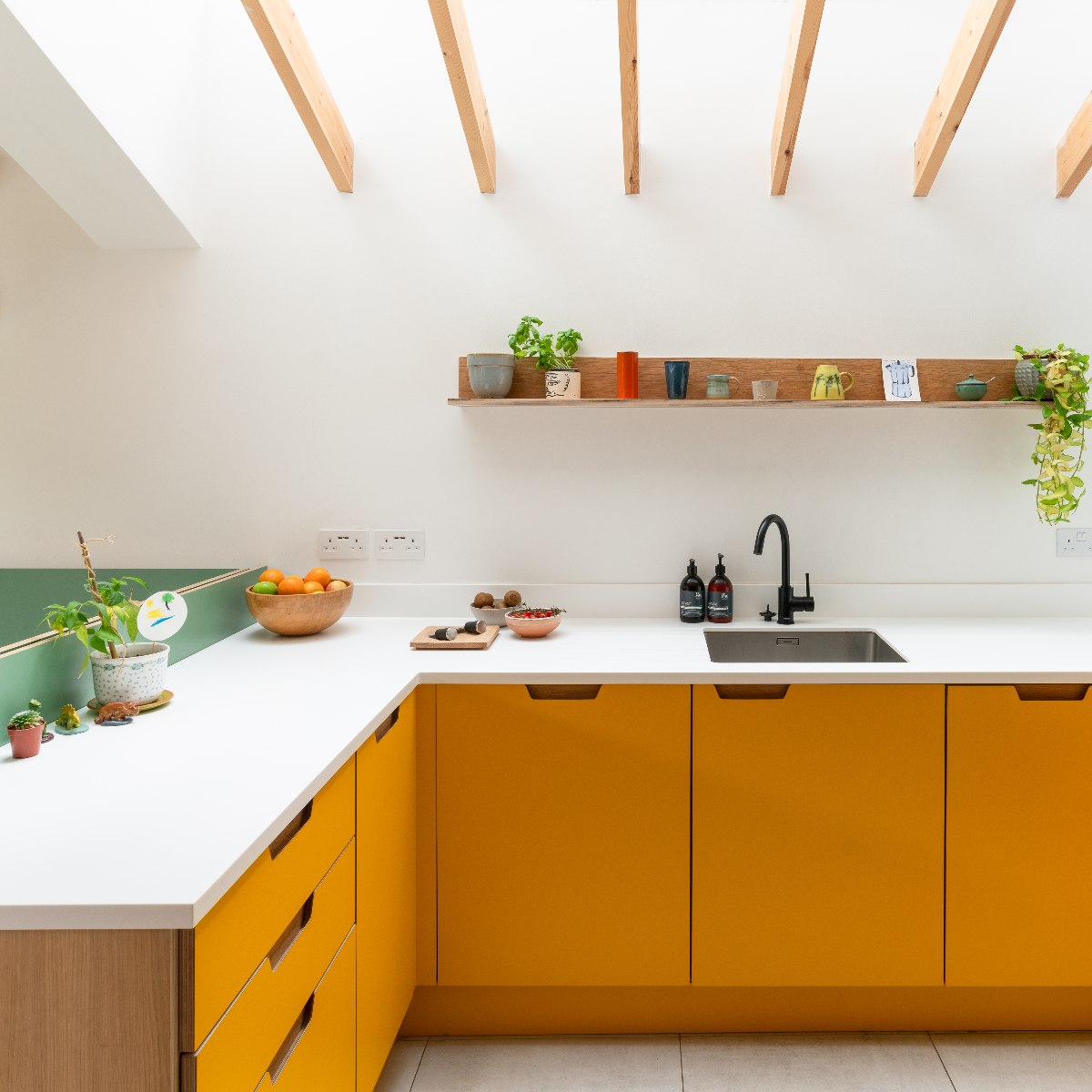 Modern kitchen with yellow cabinets, white surfaces, sink and tap, and compact open shelf under a glass roof.