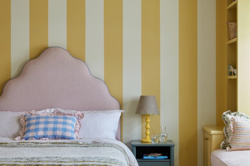 Playful bedroom with striped wall coverings, statement ceiling, a blush pink bed, a window seat.