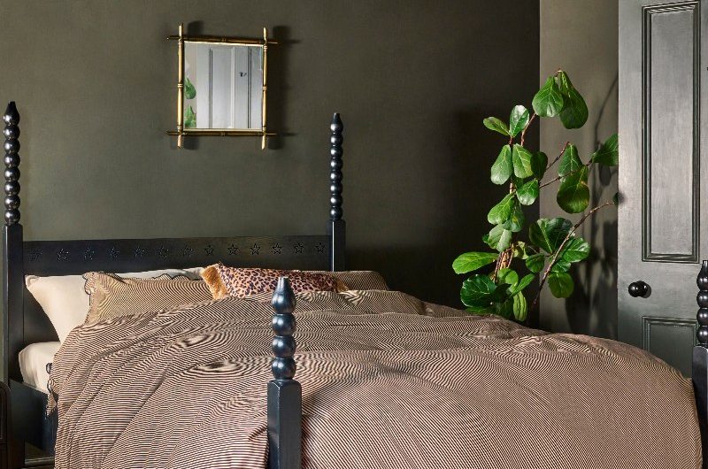 Dark green bedroom with a black, bobbin and wood bed frame, striped linen, and house plants.