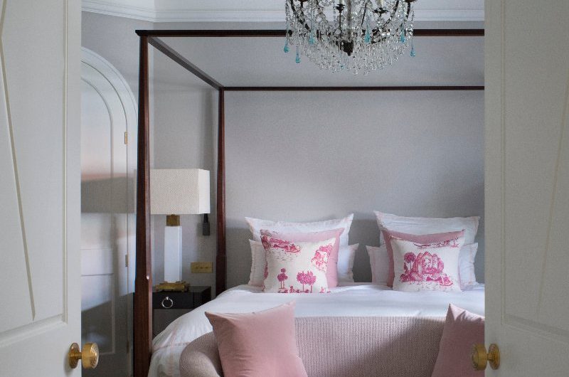 Bedroom with four-poster bed, vintage glass chandelier above and a silk rug underfoot.