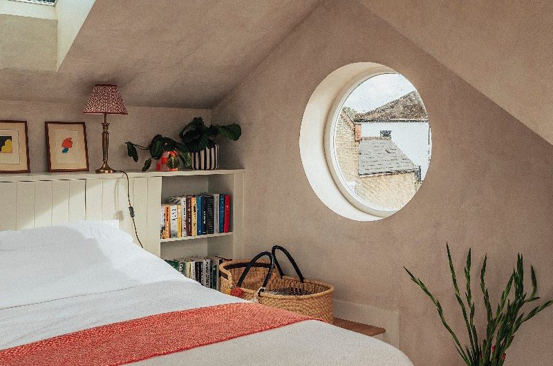 A neutral bedroom in a loft conversion with a porthole window and plastered walls.