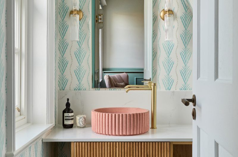 Colourful bathroom design with fluted vanity, a concrete basin, patterned wallpaper and gold tap.