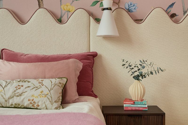 A custom wall-to-wall fitted headboard with a scalloped edge, in a soft cream bouclé fabric with pink velvet piping in a blush pink bedroom.