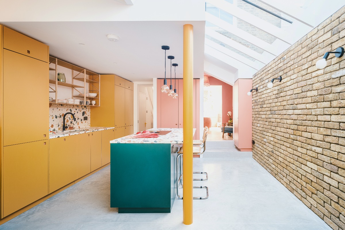 Yellow kitchen design with a matching painted structural beam and green island, topped with terrazzo surfaces.