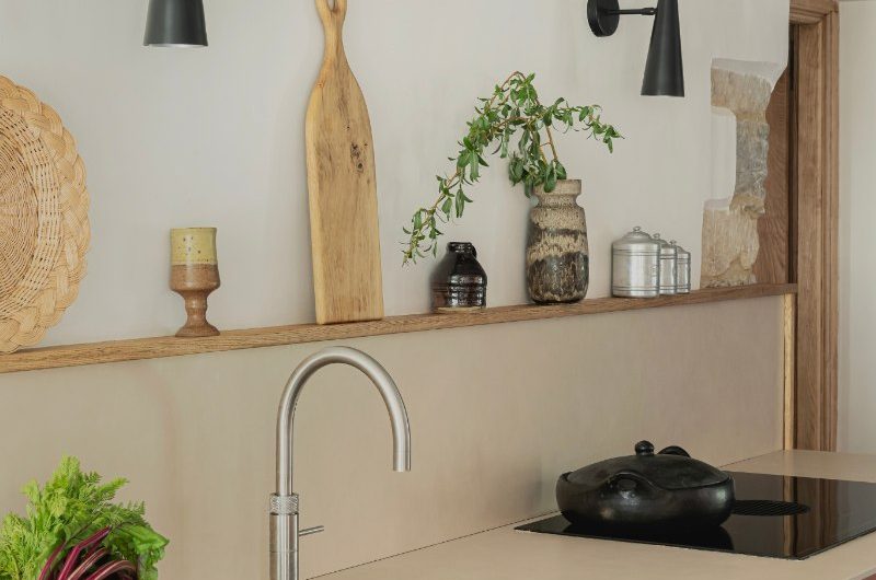 A cabinetry run with terracotta fronts, off white worktops and splashback, a think shelf, and a hob with a washing up area next to it.