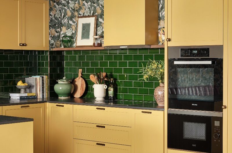 Flat with sunshine-coloured cabinets, green tiles, built-in appliances and checkerboard flooring.