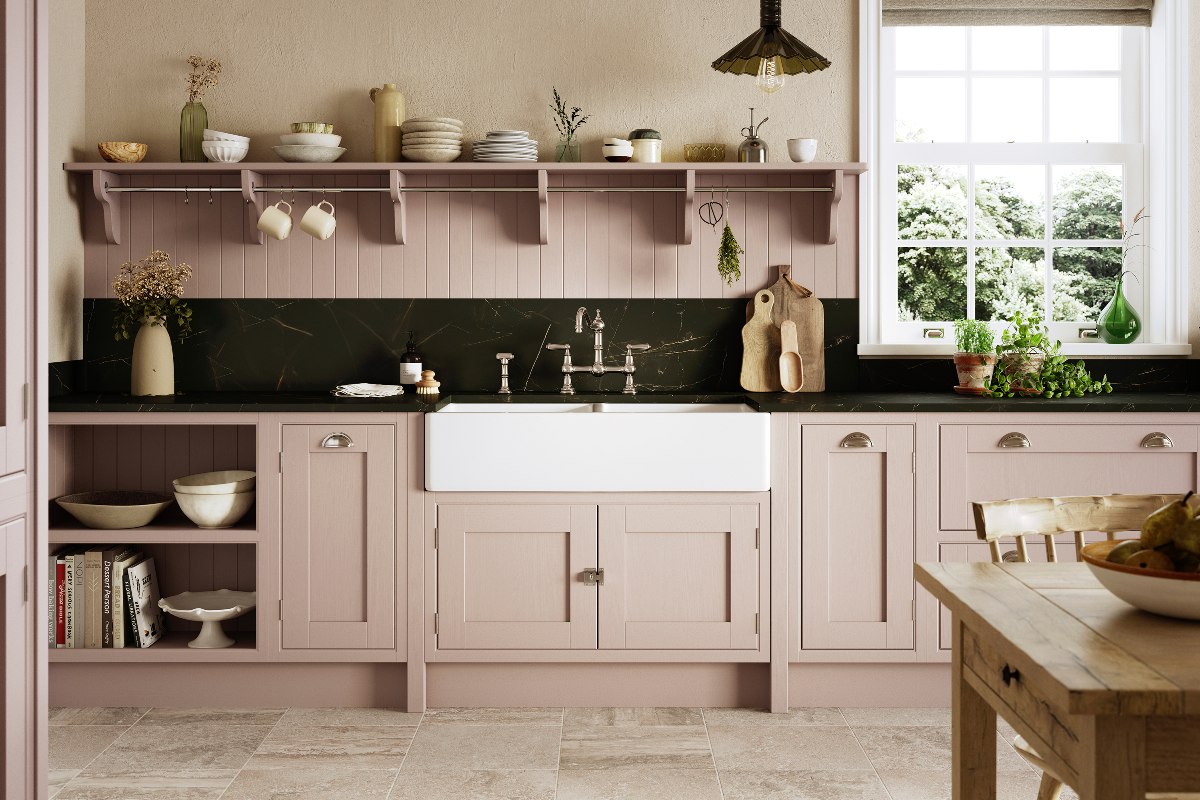 A farmhouse style space with pale pink cabinetry, dark worksurfaces, open shelving, and a large butler sink size.