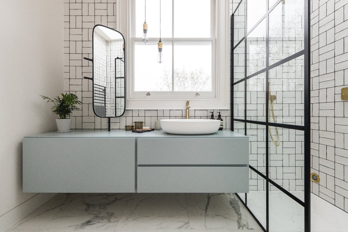 A light and bright bathroom with a vanity area placed under the window for illumination with a wall-mounted unit and matt black finishes. 