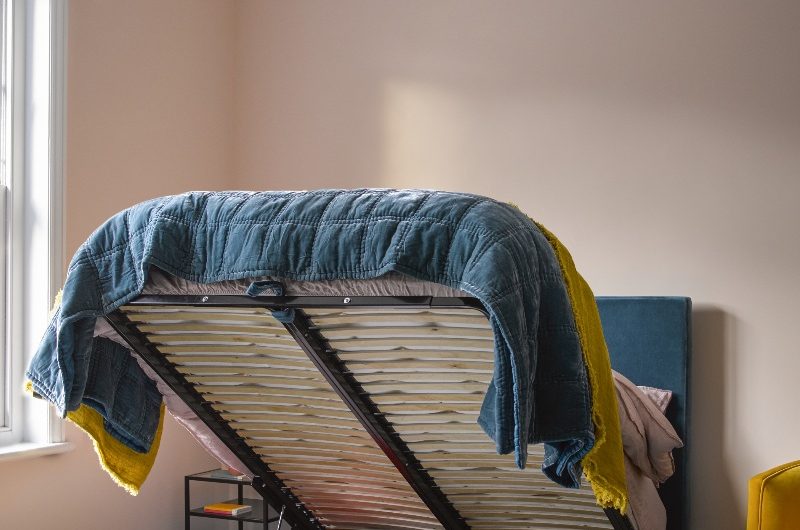 An blue velvet ottoman bed with space for cushions and throws underneath.