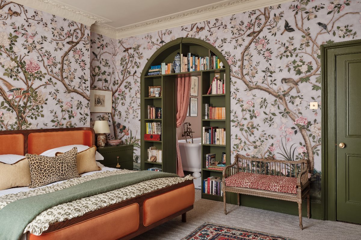 A colourful bedroom design with biophilic wallpaper, green woodwork and an adjoining ensuite through a bookcase-like entryway.