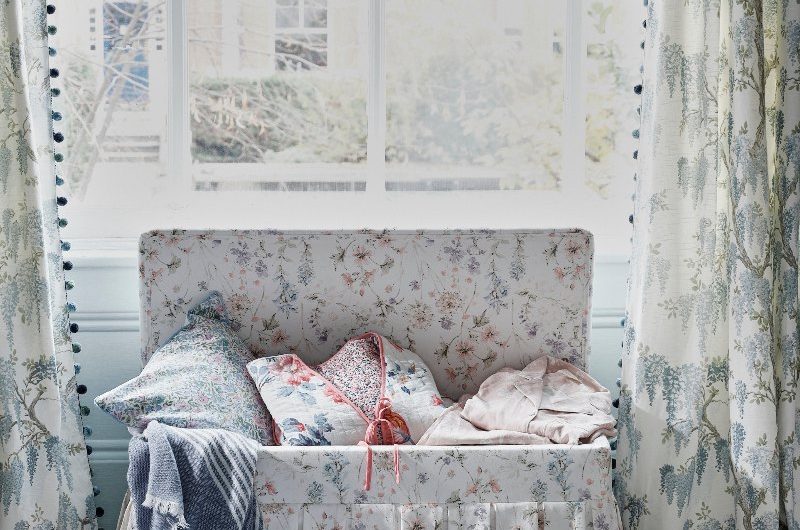 A floral ottoman storing cushions by a window.