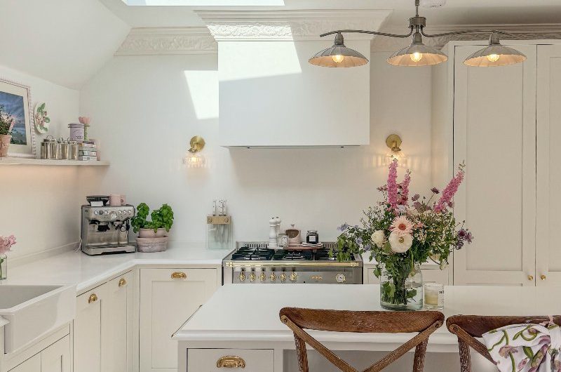 A white classic kitchen with brass handles, an island, vintage stools and layered lighting.