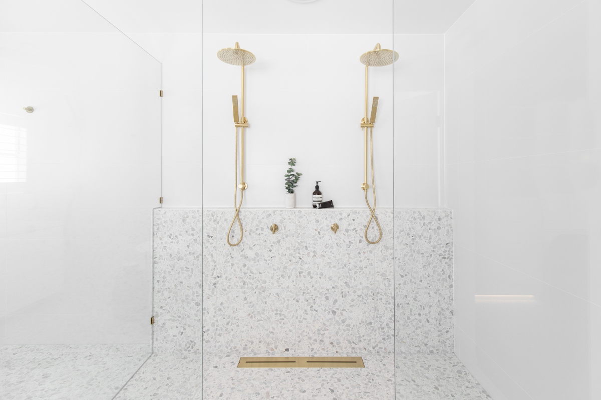 A luxury bathroom with terrazzo surfaces and gold double showers.