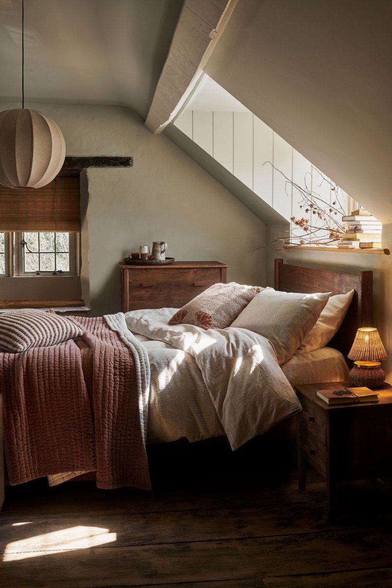 Rustic sleep space with wood furniture, wall panelling, warm lighting, and layered textiles.