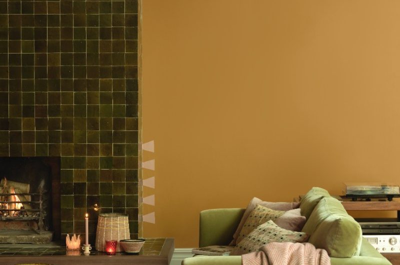 Autumn living room in a muted mustard colour with forest green tiles on the fireplace, an olive green sofa, and wood furniture.