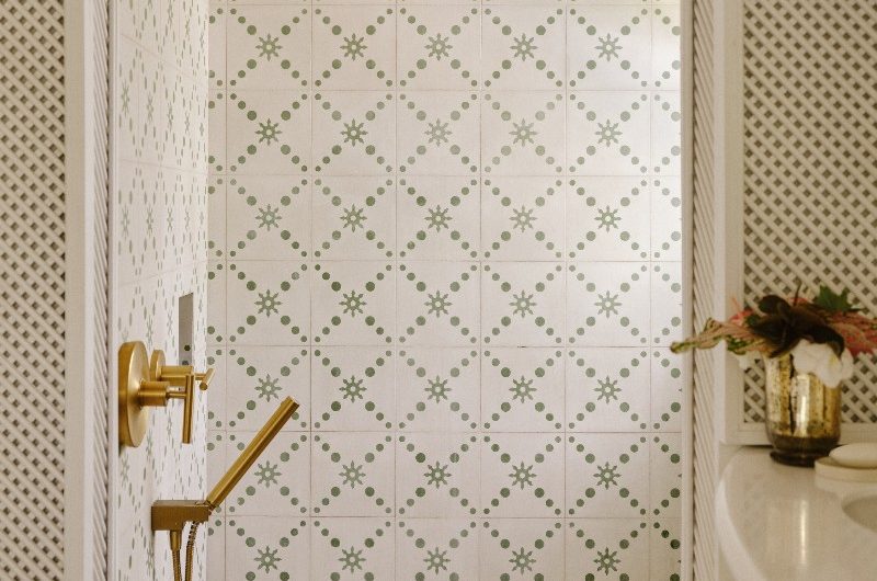 Shower area with green and white patterned tiles and bronze brassware.