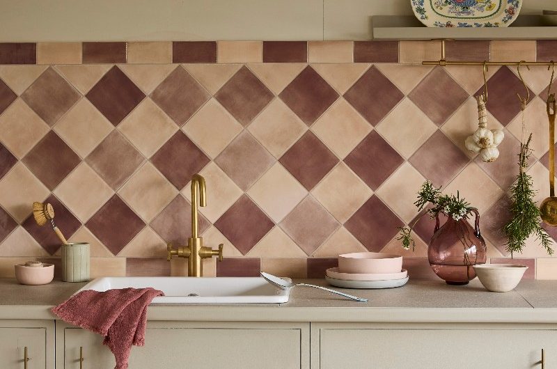 Kitchen washing up zone with diamond-shaped tiles in neutral colourways, a brass tap and white sink, and sleek cabientry.