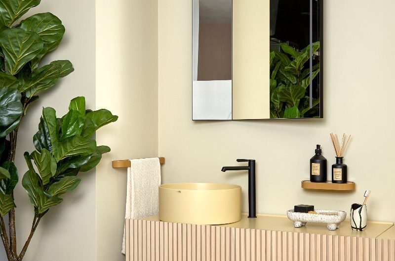 Modern bathroom with a butter yellow basin on top of a wood wall-mounted unit, with a black tap and minimalist decor.