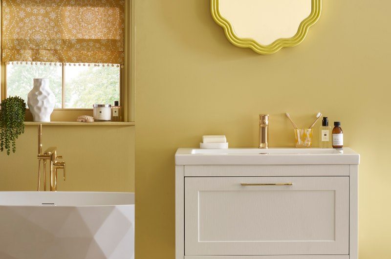 A vibrant yellow scheme with checkerboard flooring, a textured tub, a wall-mounted vanity and quirky mirror.
