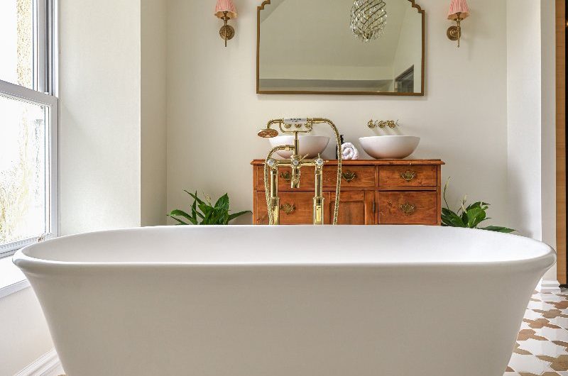 Spa-like bathroom design with patterned flooring, a freestanding tub, gold bath filler, a vintage vanity with double basins and a chandelier.