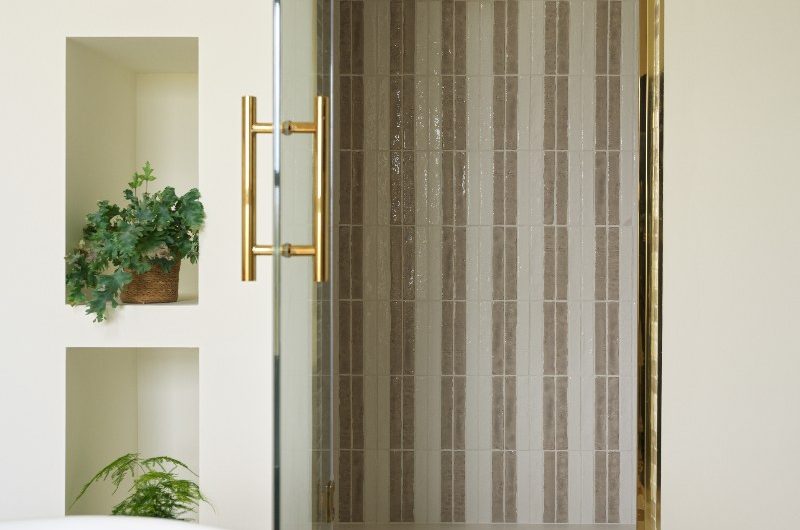 A striped shower with a gold enclosure panel and matching brassware.