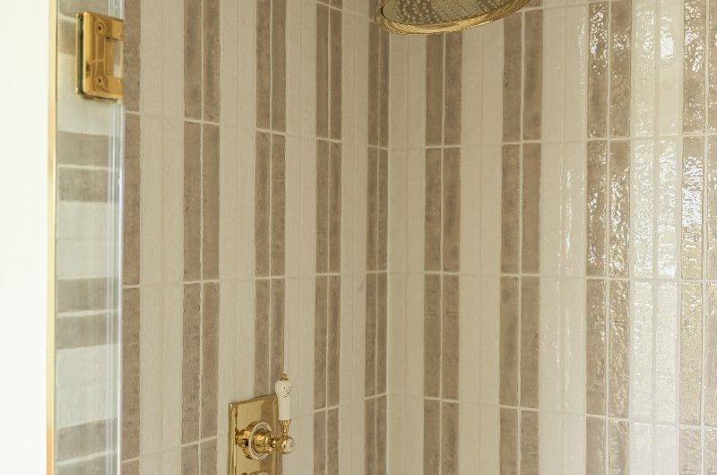 Close-up at the striped shower with cream and white tiles and gold brassware.
