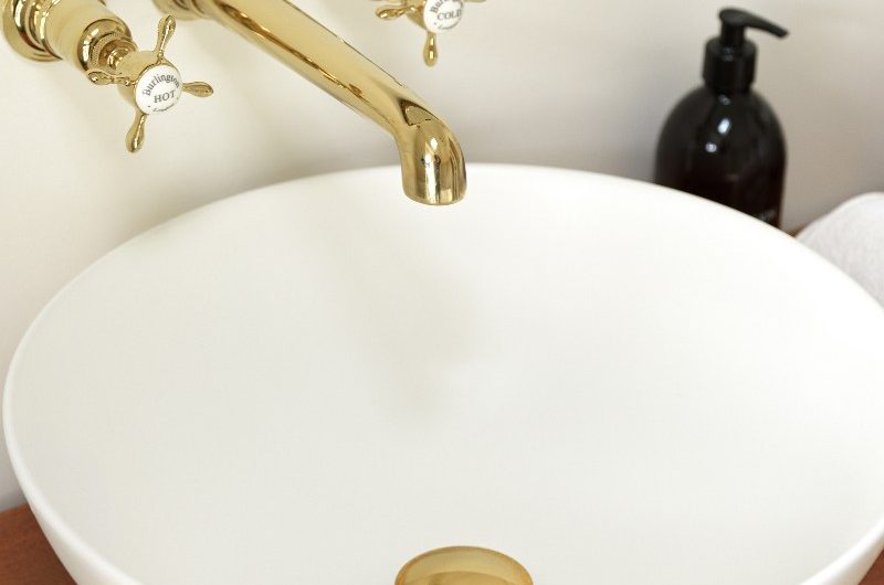 Close-up at the basin with gold tap, mixers and waste.