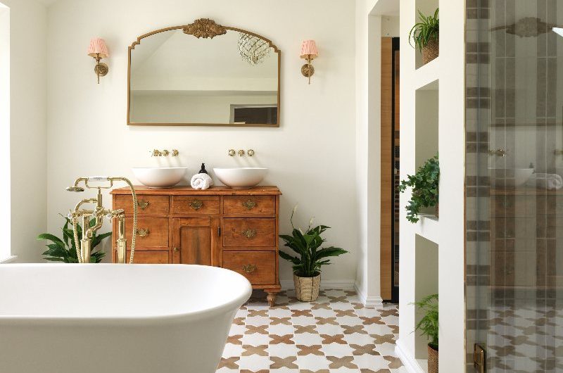 Spa-like bathroom design with Moroccan-inspired flooring, a freestanding tub, a vintage vanity with double basins, and gold finishes.
