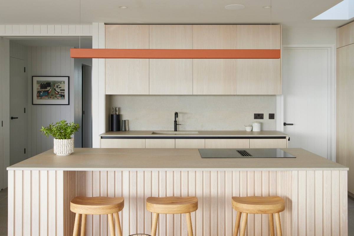 A simple wood kitchen design with an island that has a built-in hob and breakfast bar with three wood stools.