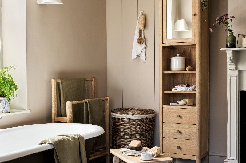 Country bathroom trend for Autumn Winter 2025 with classic wall panelling, wood furniture, wood towel holders, rattan laundry basket, and a freestanding tub.