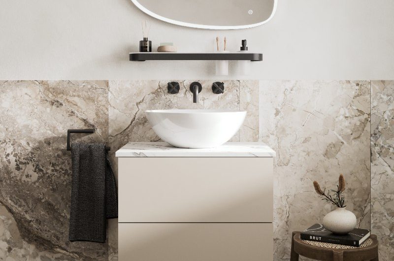 Modern scheme with floorstanding vanity, large format veiny tiles, a wall-mounted shelf with accessories and a pebble shaped mirror.