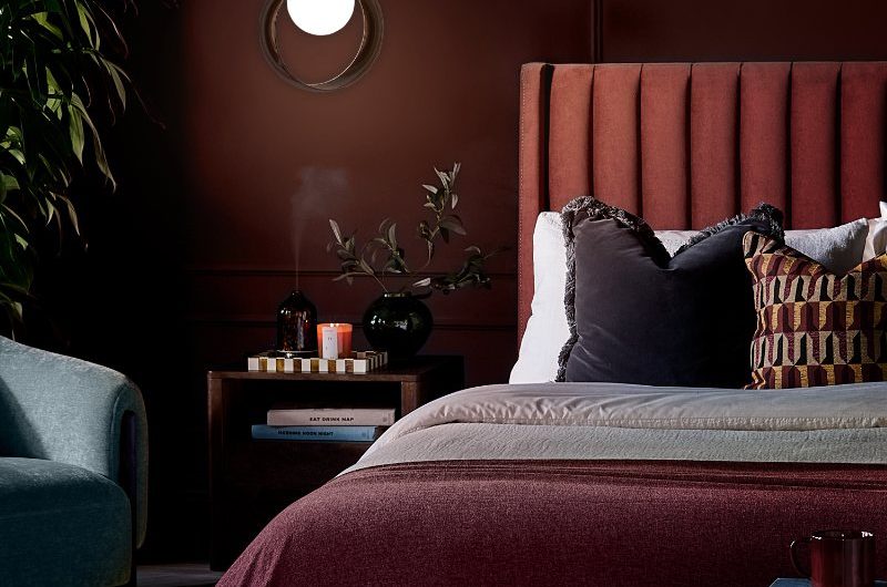 Burgundy autumn bedroom design with a velvet headboard, dark bedding, wood side table, and mood lighting.