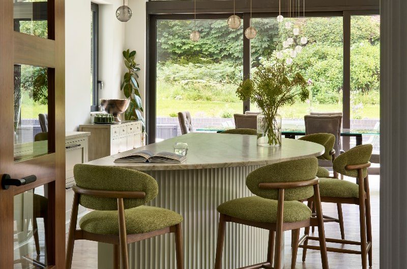 A curved island with a fluted finish, a veiny work surface extended as an overhang and tactile green chairs.