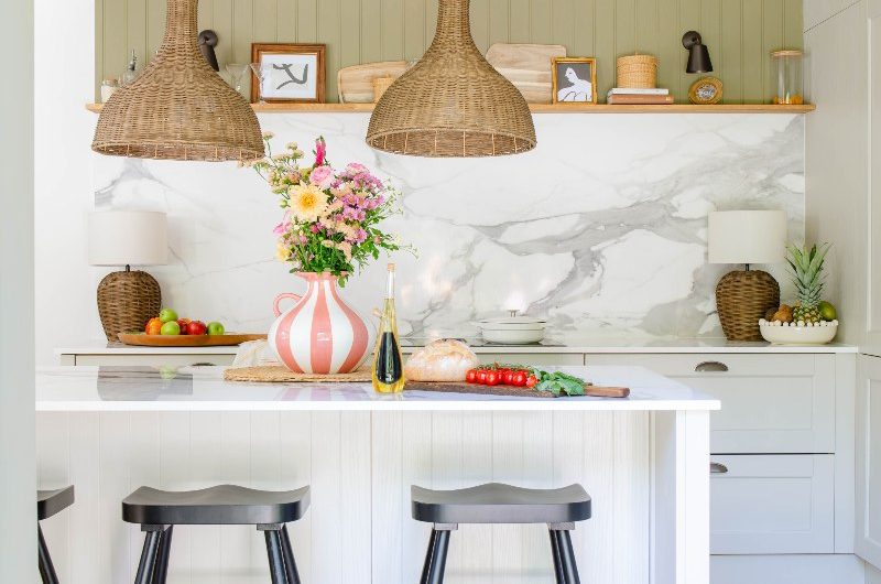 Kitchen makeover with light taupe cabinetry, sage green panelling, marbled work surfaces, an island with seating and pendant lights above it.