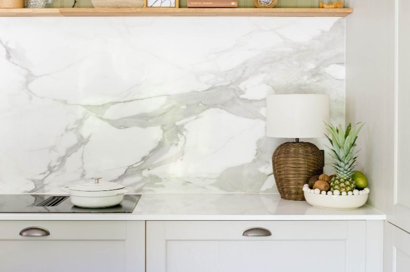 A closeup at the cooking zone with veined quartz worktop and splashback, a venting hob and open shelf for decor.