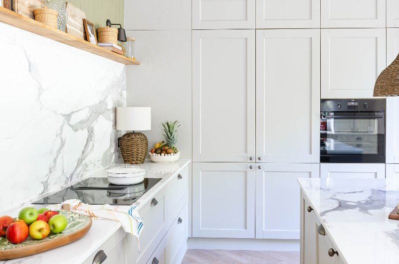 A neutral kitchen makeover with classic cabinetry, veined surfaces, wood flooring, and open shelving.