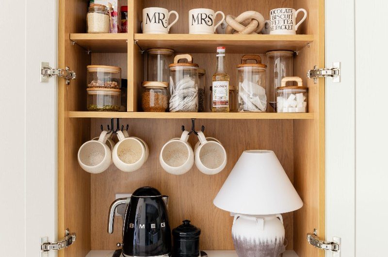A breakfast cupboard with a kettle, mugs, and a lamp.