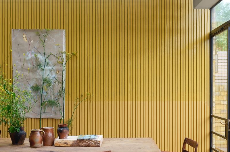 Dining room interior design with yellow wall panelling, wood table, and yellow and wood upholstered chairs.