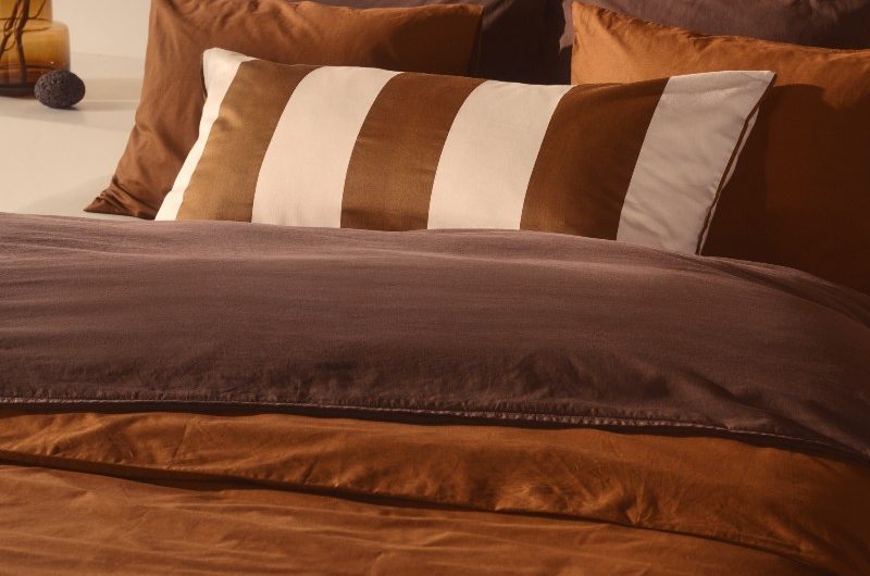 Brown bedding with a striped cushion, wood panelling behind it, and autumn decor.