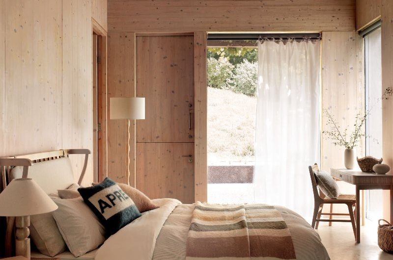 Ski chalet-inspired bedroom with an autumn feel, drenched in wood on the walls, ceiling and floors, with blonde wood furniture and neutral bedding.