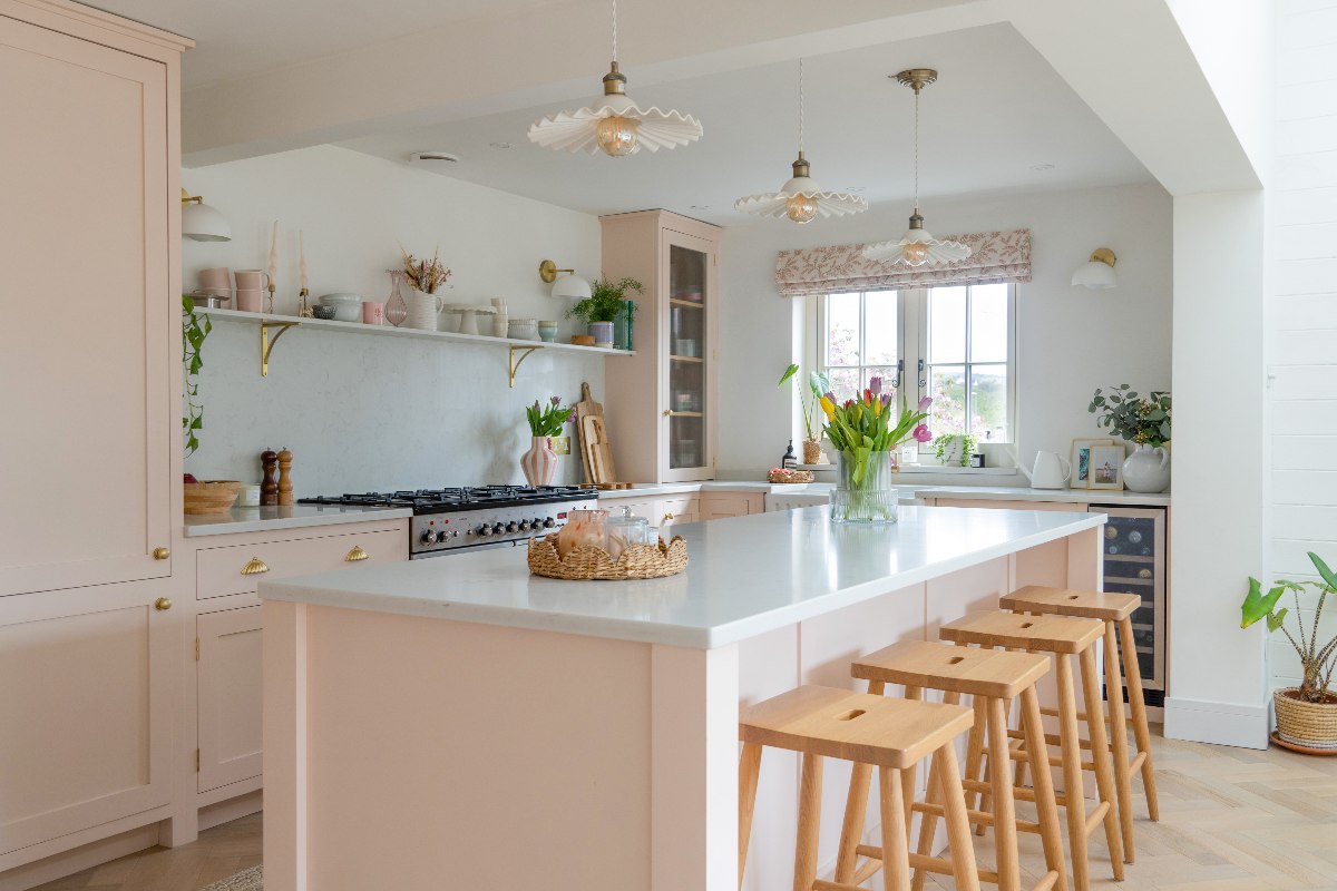 Pink kitchen design with a breakfast bar with four chairs, white surfaces, and chic decor.