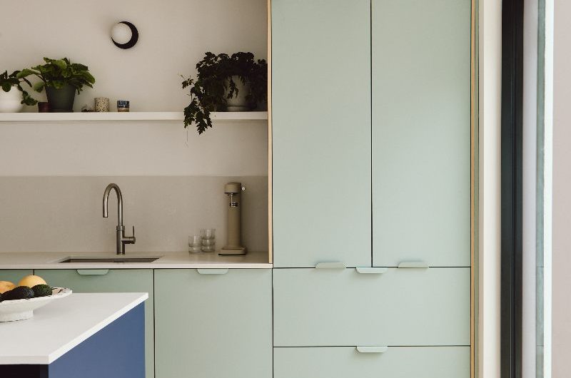 Modern design with pastel green cabinetry, white surfaces, a blue island and jute rug near the glazing.