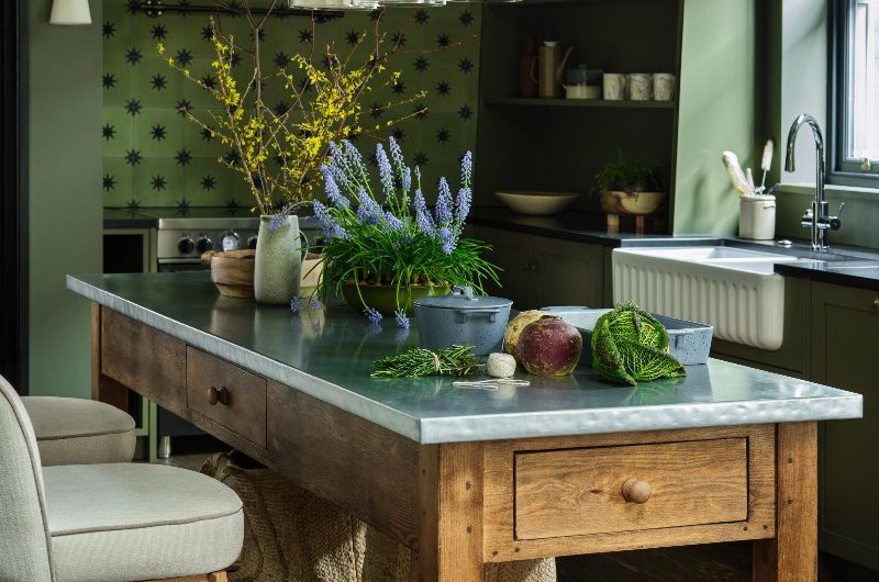 Green kitchen with a wood chef's table with bar stools and pendant lighting above it.