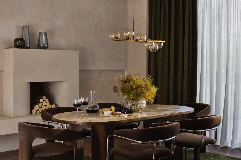 Autumn dining room with brown velvet seating, green rug, wood flooring, and neutral plaster on the walls.
