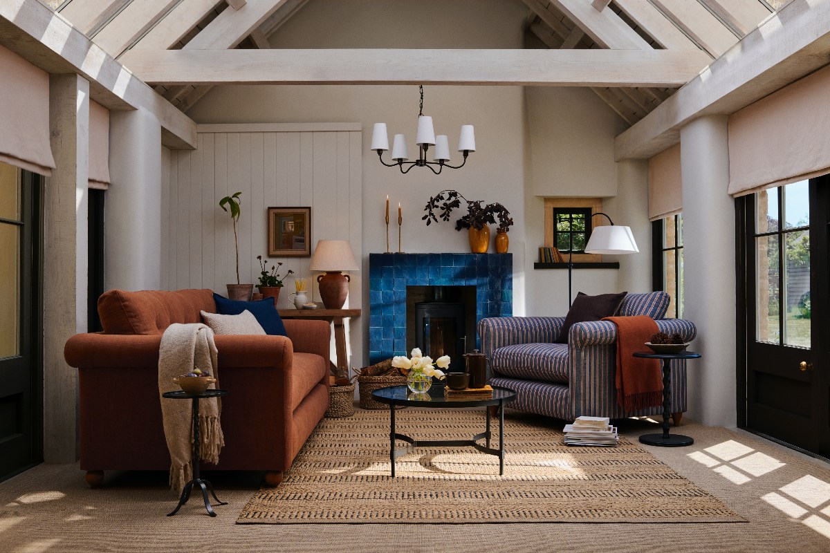 Living room with a rust-coloured sofa, a striped armchair, tiled fireplace, wood beams, and antique and forged metal decor.