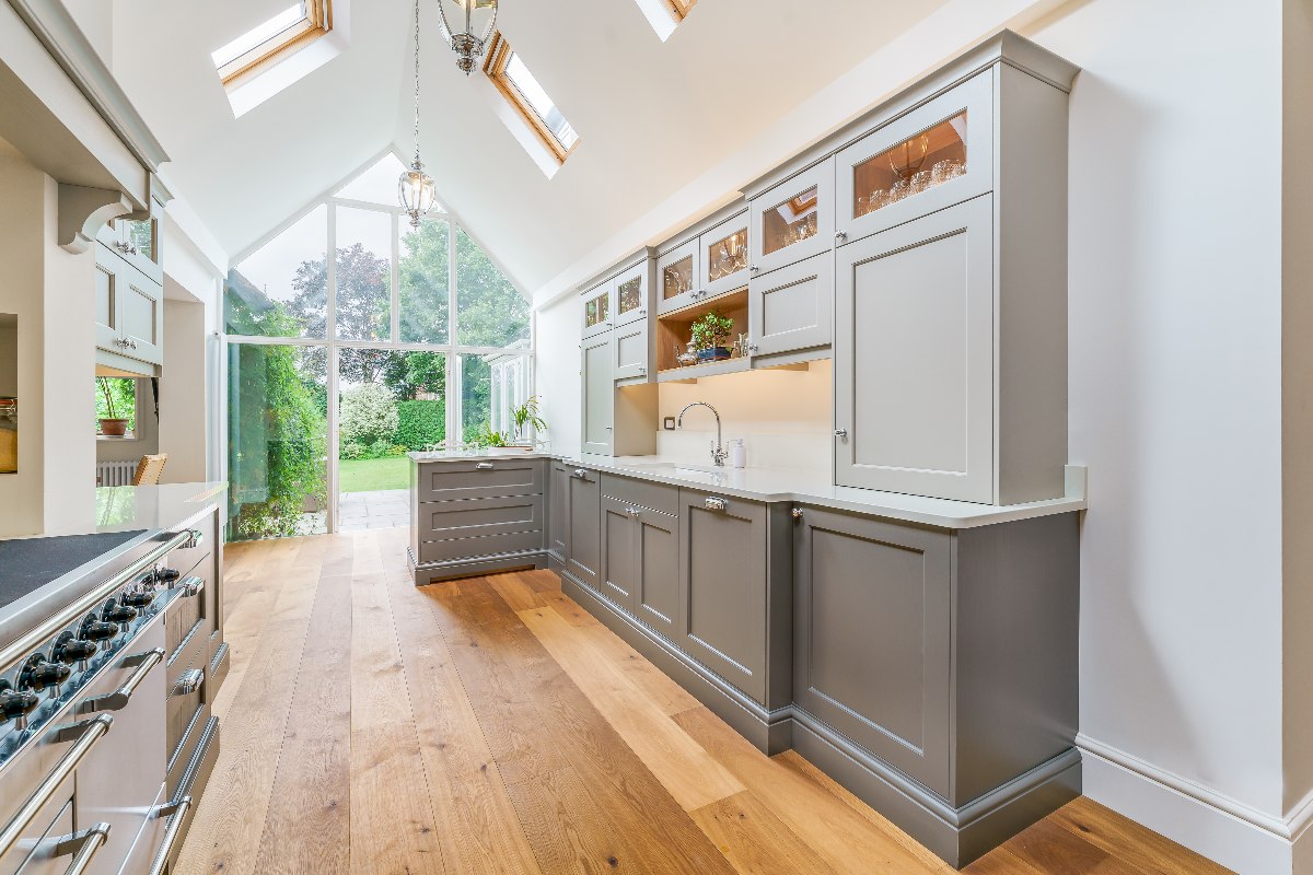 An open-plan kitchen with a wood floor, skylights, grey cabinetry, and indoor-outdoor connection.