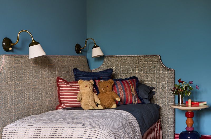 Kids' bedroom with a single bed dressed in striped linen, with wall lights, and a quirky side table.