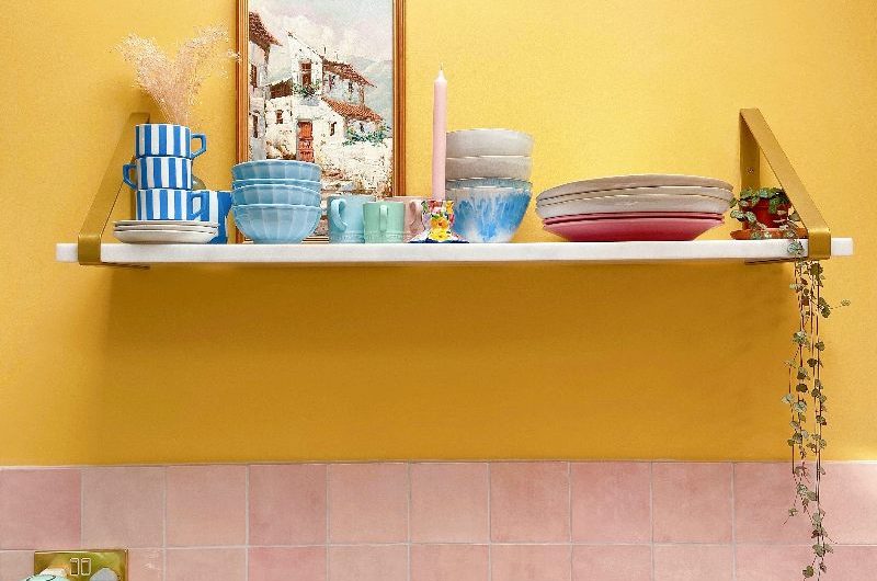 Cooking zone in a kitchen with a gas hob, marbled worktops, pink tiles, lemon-coloured paint and an open shelf.